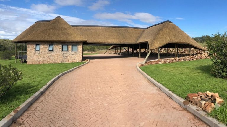 Home A premium large-scale thatched roof structure featuring custom timber pole framing and stone masonry integration under a clear blue sky.