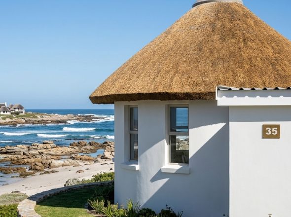 Round coastal resort chalet rondavel with a clean thatched roof overlooking the ocean and rocky shoreline