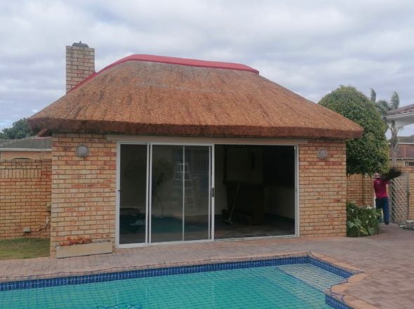 Projects Brick pool house with large glass sliding doors featuring a freshly combed Cape reed thatched roof