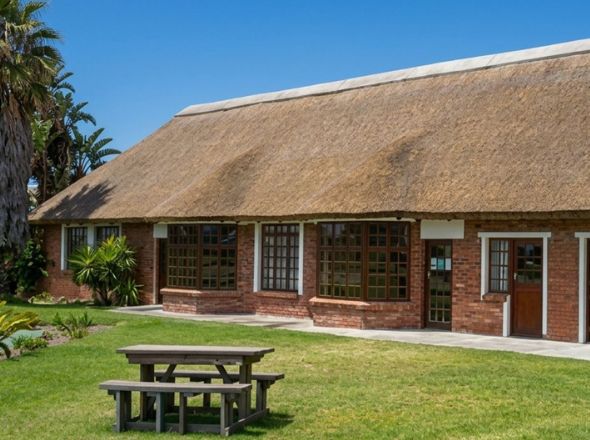 Projects Classic facebrick residential home with a premium large-span thatched roof and a wooden picnic bench on the front lawn