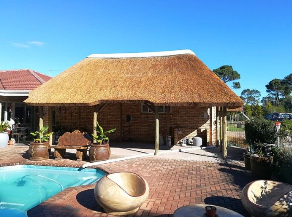Projects Open sided freestanding thatch lapa supported by heavy timber poles on a paved patio next to a swimming pool