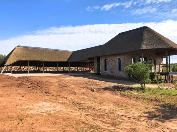 Projects Large-scale game reserve reception building showing expansive interconnected thatched roof wings and natural rock masonry construction