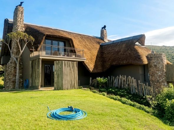 Premium thatched roof installation on a luxury double-story bush lodge featuring natural stone chimneys and custom timber lath fencing