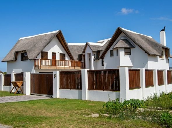 Premium multi-story residential thatched roof construction with custom timber fencing and balcony railing in St Francis Bay