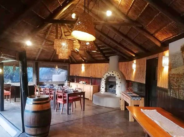 Projects Luxury safari lodge indoor dining area featuring an exposed structural timber pole roof, woven chandeliers, and a stone fireplace